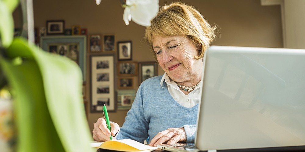 Senior woman at home with laptop and notebook