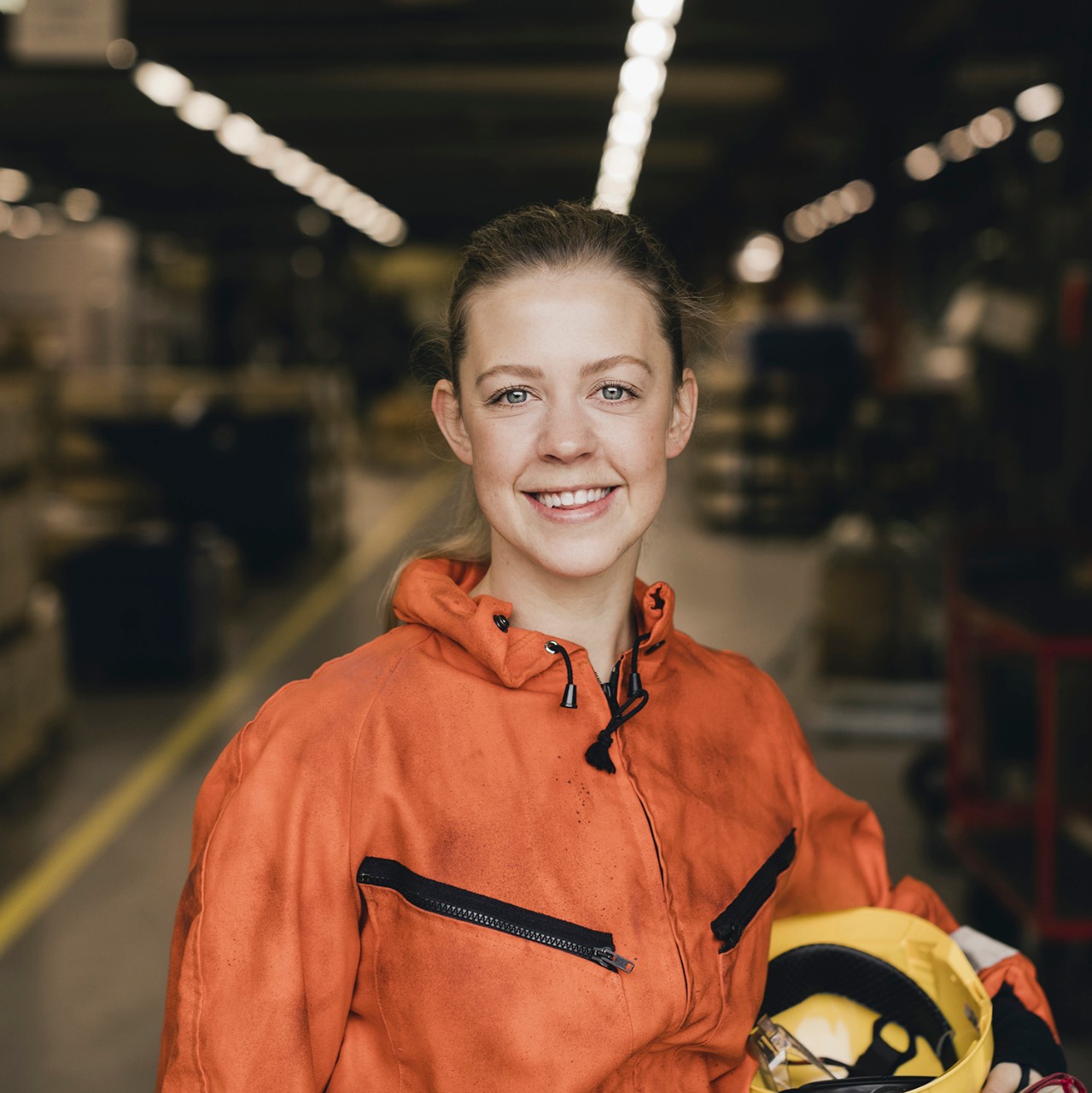 Smiling young female worker in orange protective workwear at factory