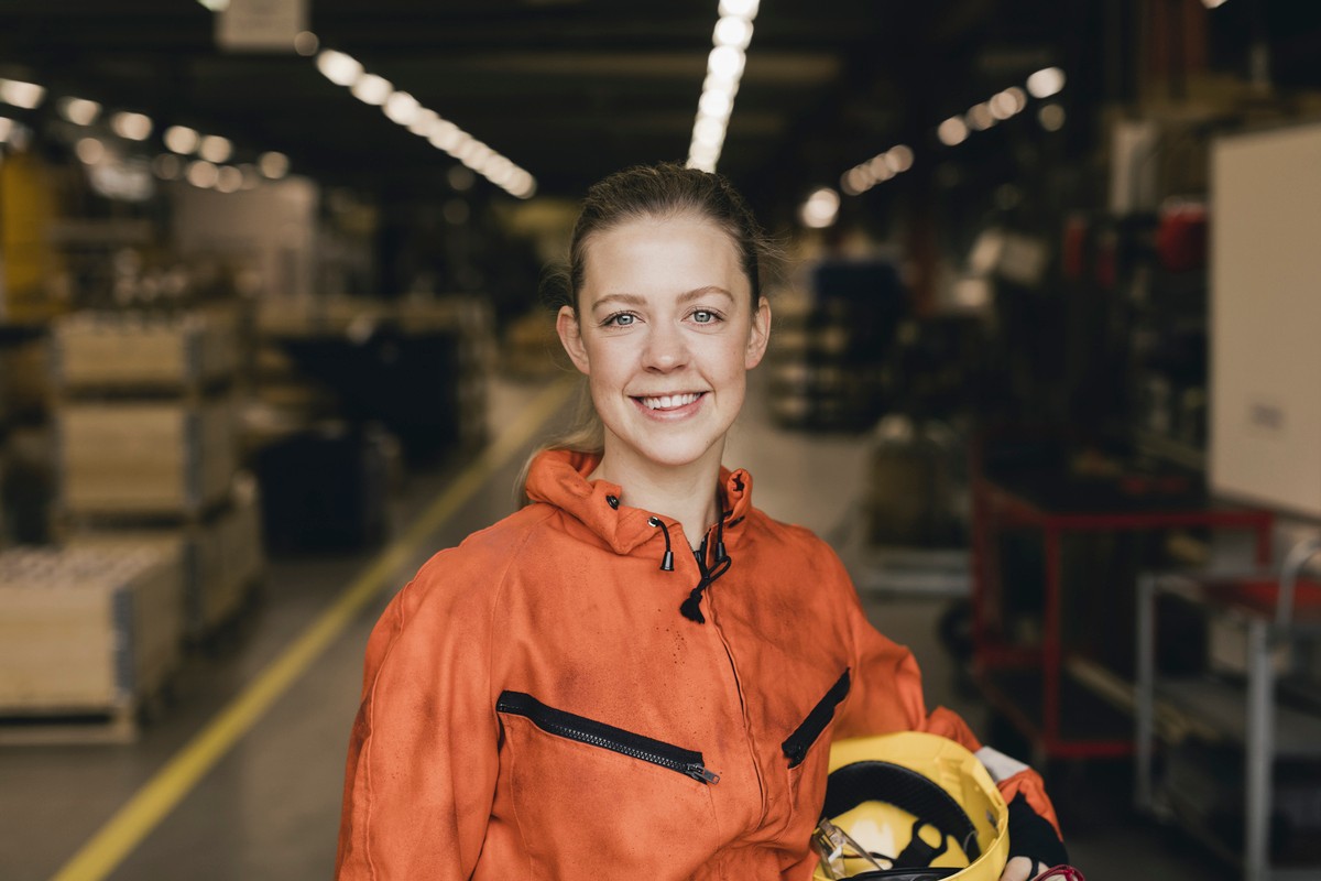 Smiling young female worker in orange protective workwear at factory