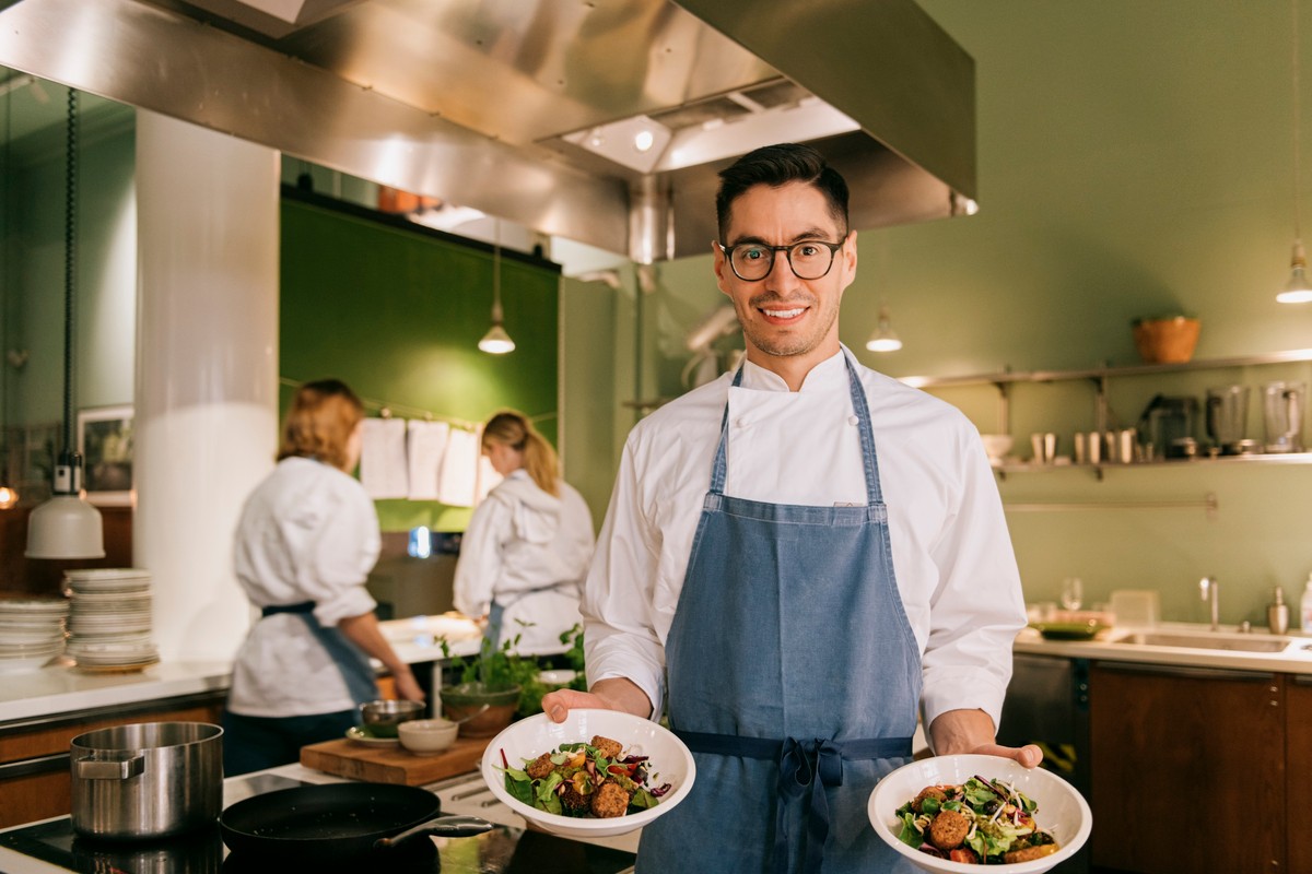 Smiling male chef holding food bowls while standing in restaurant kitchen