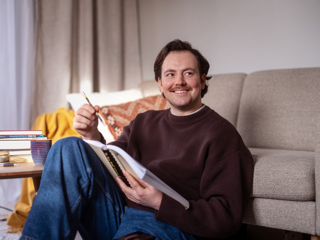 Mann sitter på gulvet foran en sofa og skriver i en bok